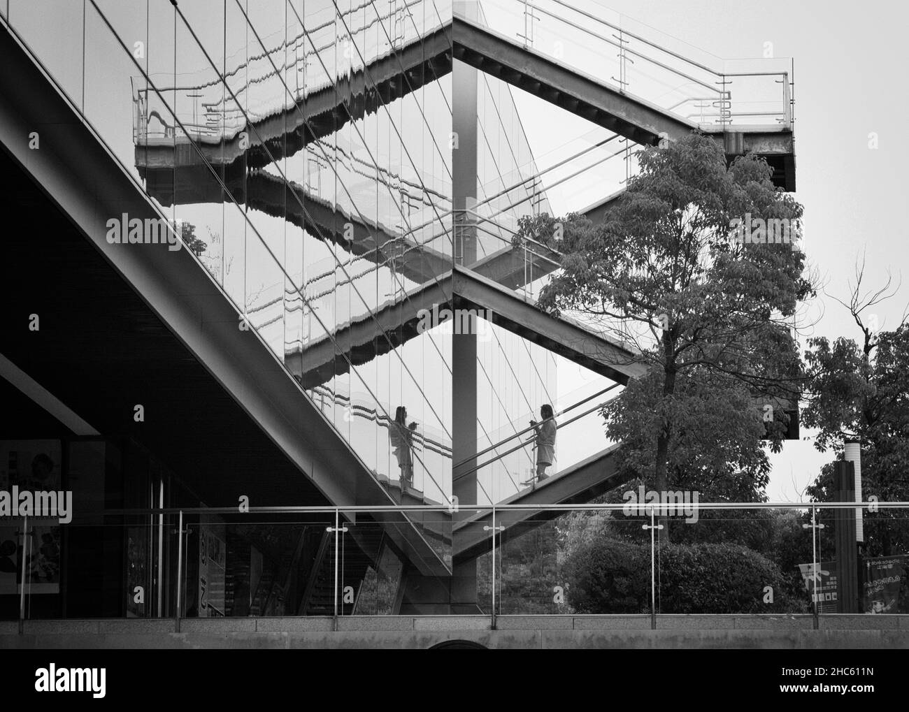 Foto di una donna che cammina lungo le scale riflessa nella finestra di un alto edificio nella foto dal basso, in un complesso di uffici, Shang Foto Stock