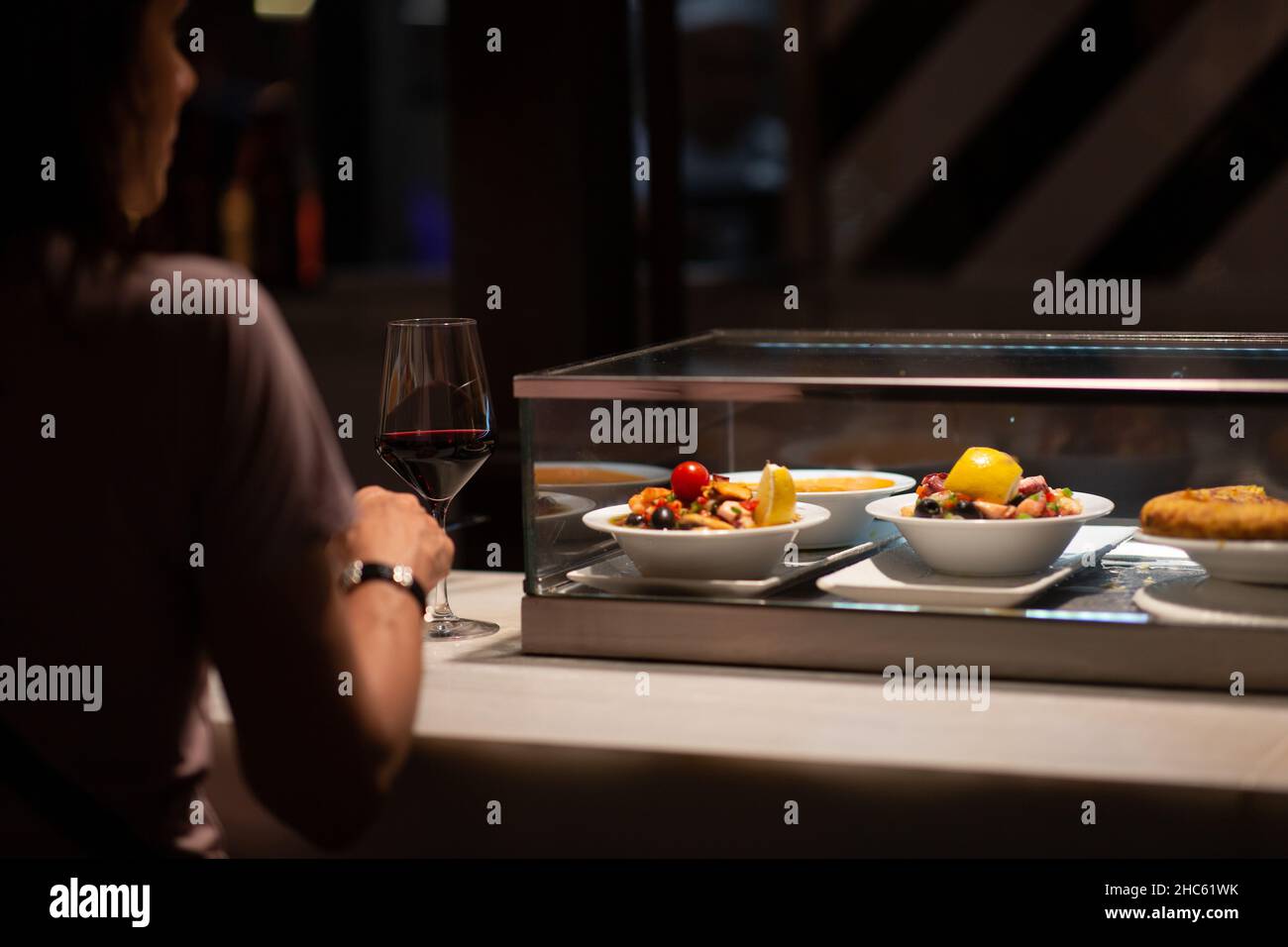 Vista posteriore di una signora che si gode la sua serata con un bicchiere di vino rosso e piatti del ristorante Foto Stock