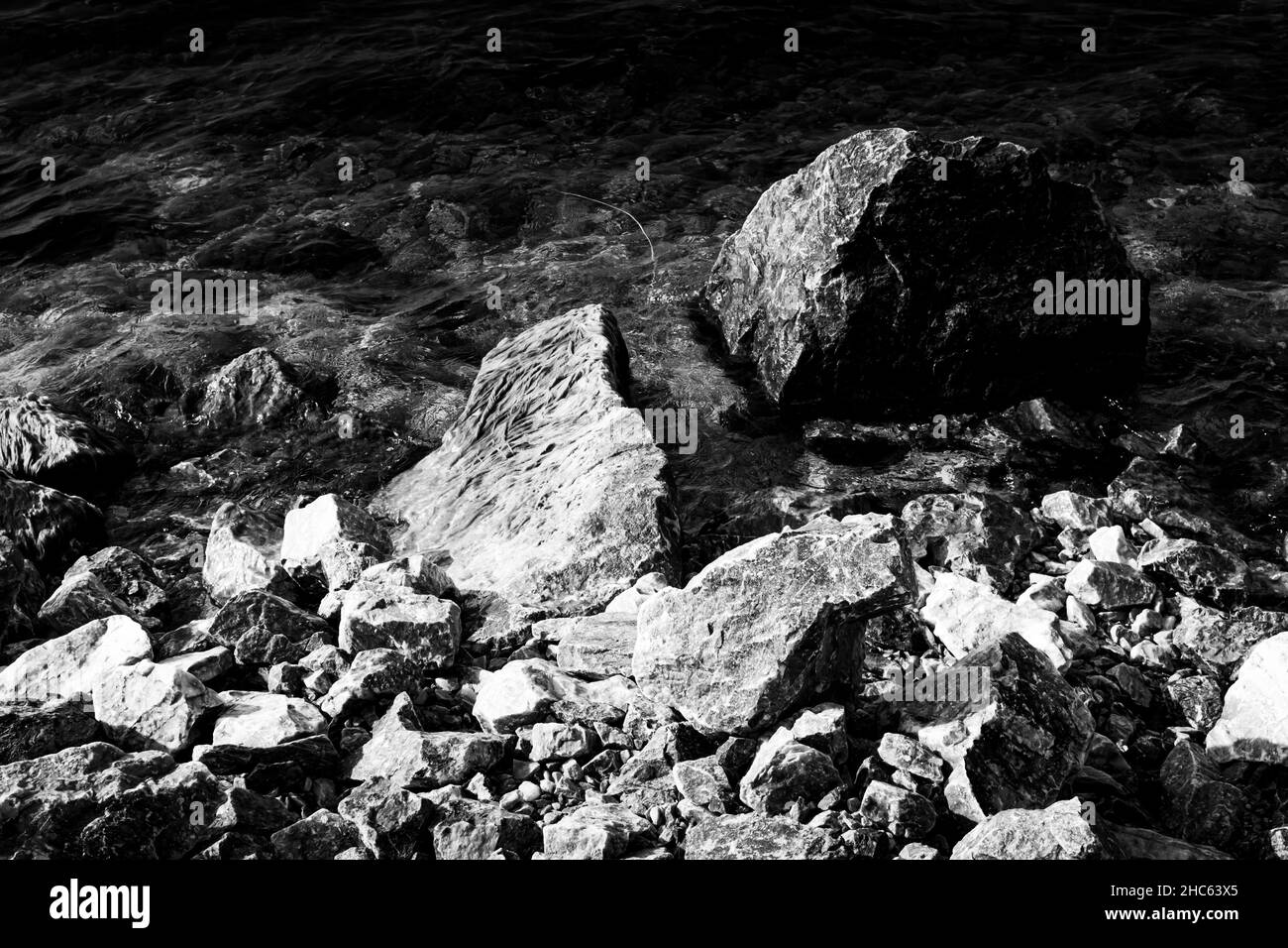 Scala di grigi ad alto angolo di rocce grandi e piccole in un fiume Foto Stock