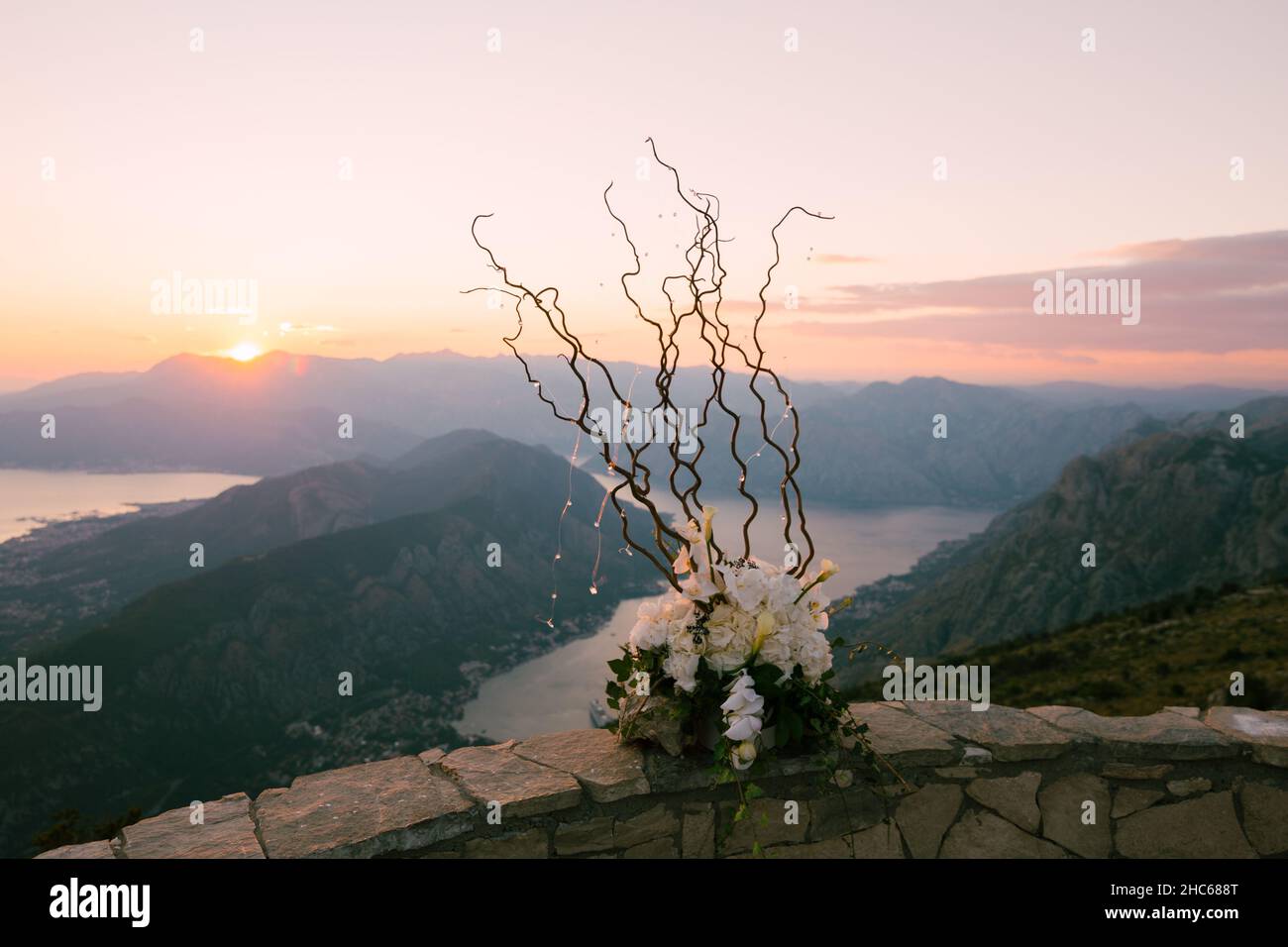 Bouquet di fiori decorati con rami ondulati si erge su un recinto di pietra sullo sfondo delle montagne e del mare Foto Stock