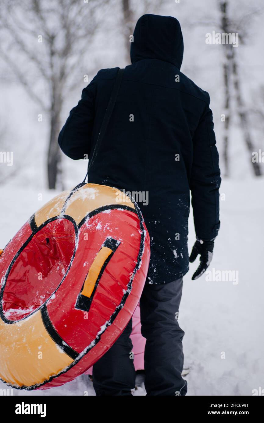 Primo piano foto di femmina russo capretto non visto dietro il padre con slitta che va su collina per scivolare giù nella neve nella foresta. Sfondo sorprendente pieno di bianco Foto Stock