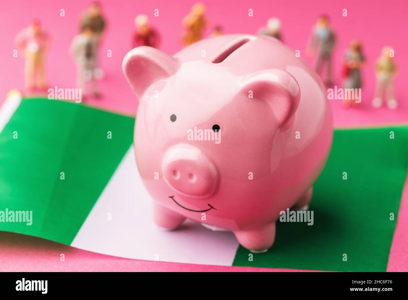 Piggy banca, bandiera nigeriana e giocattoli di plastica uomini su uno sfondo colorato, il concetto sul tema del reddito della popolazione della Nigeria Foto Stock