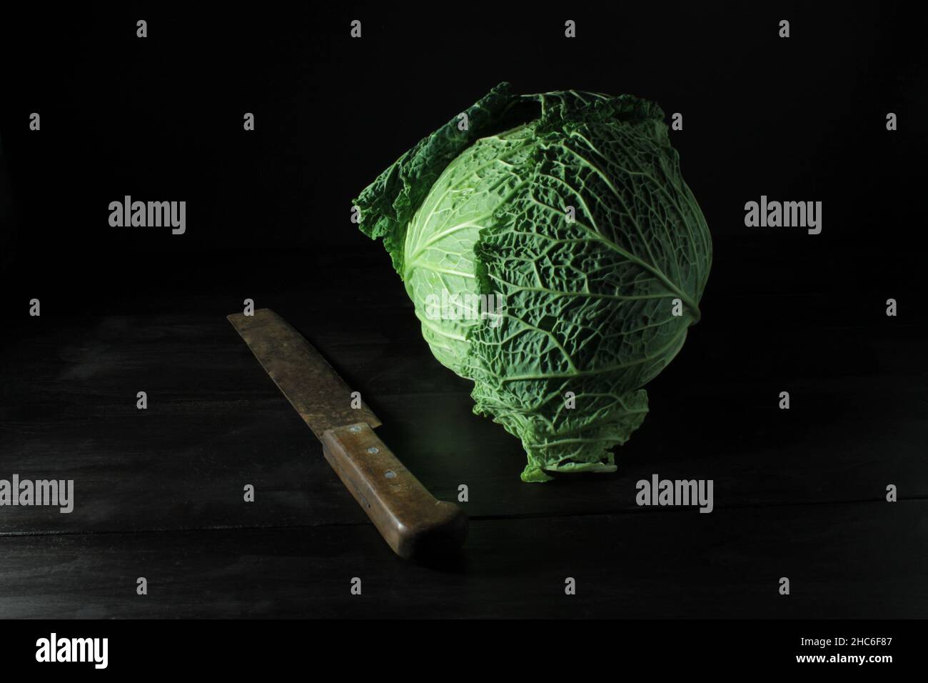 Primo piano di un vivace cavolo verde accanto a un coltello da cucina su sfondo nero Foto Stock