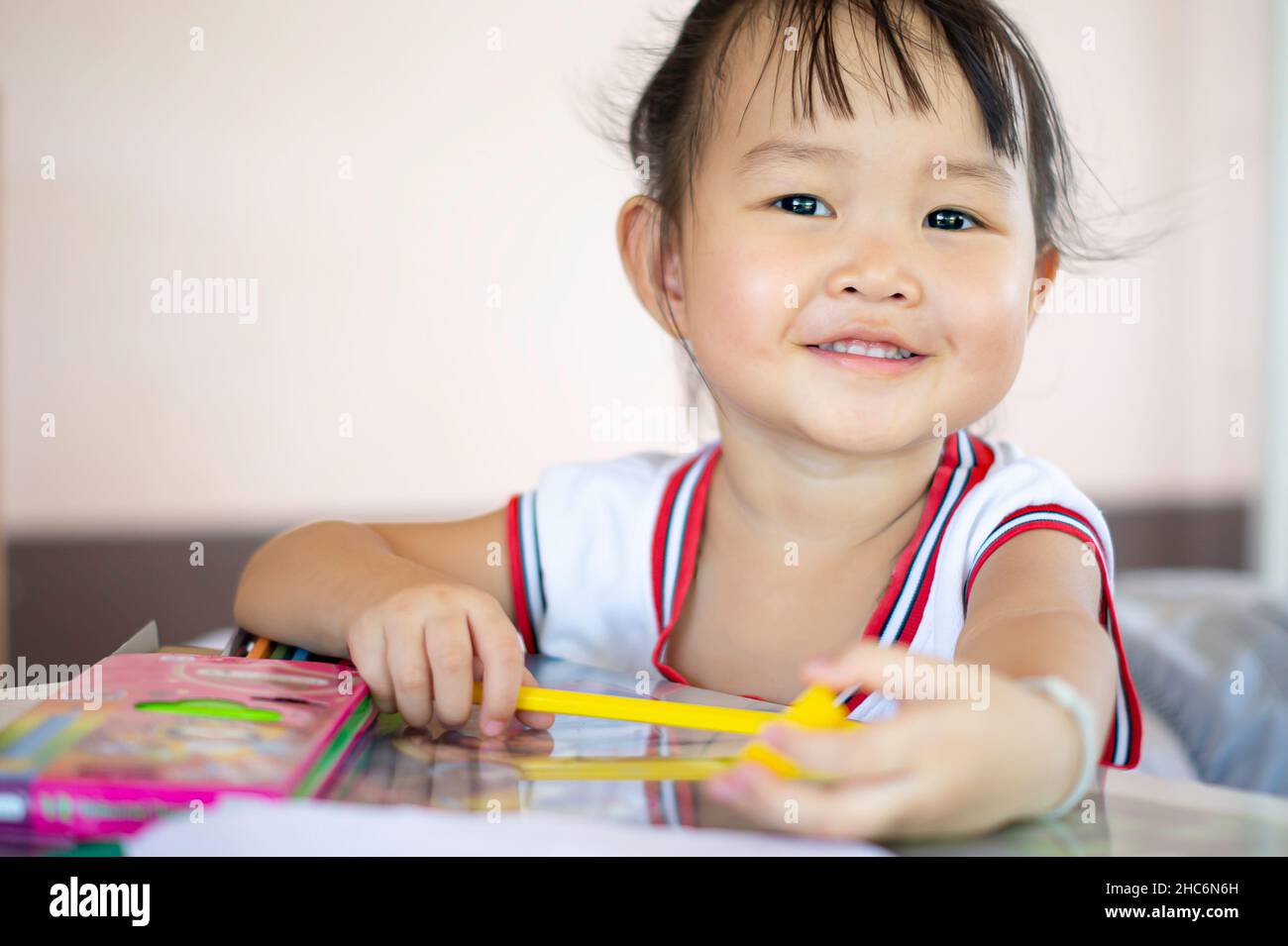 Una giovane femmina asiatica toddler con capelli neri sorride e mostra bella teeth.she felicemente con matite colorate.and spazio di copia. Foto Stock