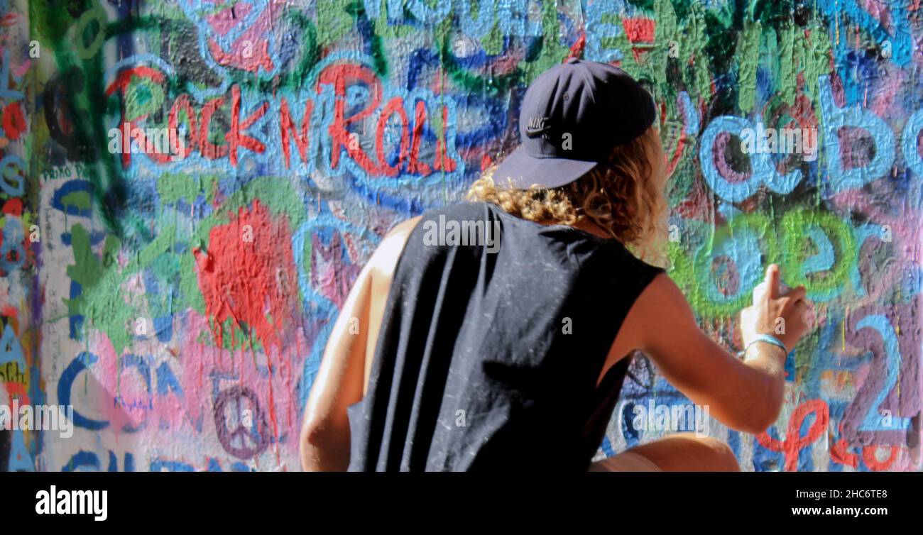 Vista posteriore di un giovane ragazzo che dipinge graffiti sul muro di John Lenon a Praga, Repubblica Ceca. Concetto di viaggio di strada. Spazio copia. Foto Stock