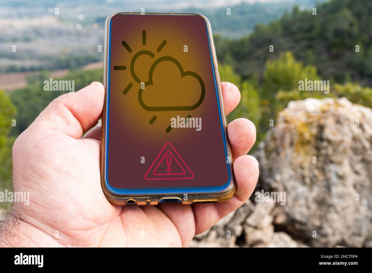 Mano maschile che tiene un telefono con l'app meteo sullo schermo e paesaggi sullo sfondo Foto Stock