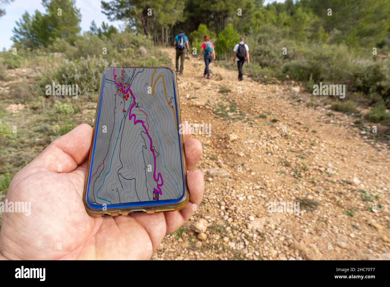 Mano maschile che tiene un telefono con la mappa trekking sul suo schermo e gli escursionisti sullo sfondo Foto Stock