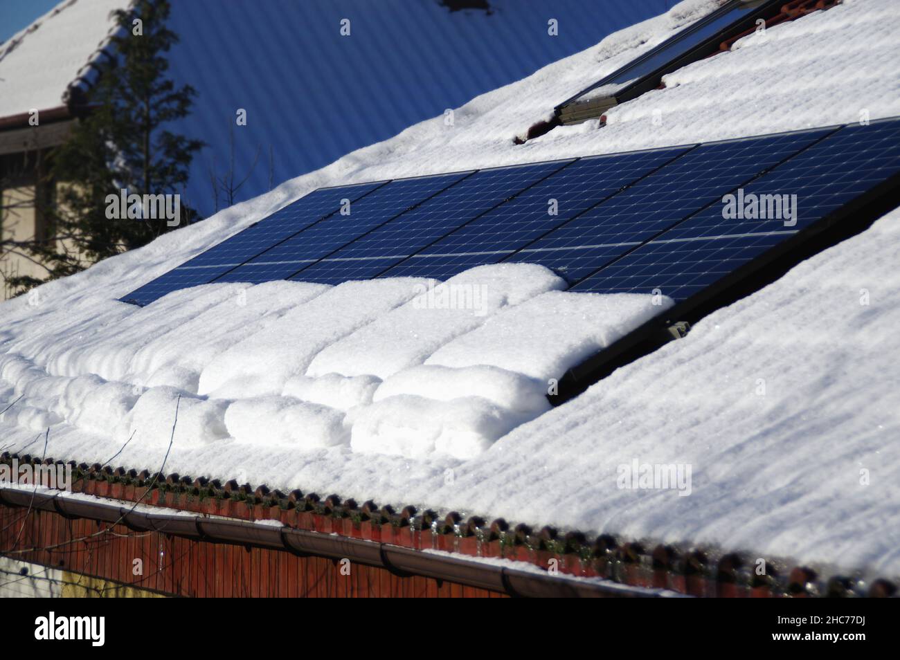 Pannelli solari ricoperti di neve. Installazione di energia elettrica fotovoltaica sul tetto della casa durante la stagione invernale in una giornata di sole. Energia alternativa pro casa Foto Stock