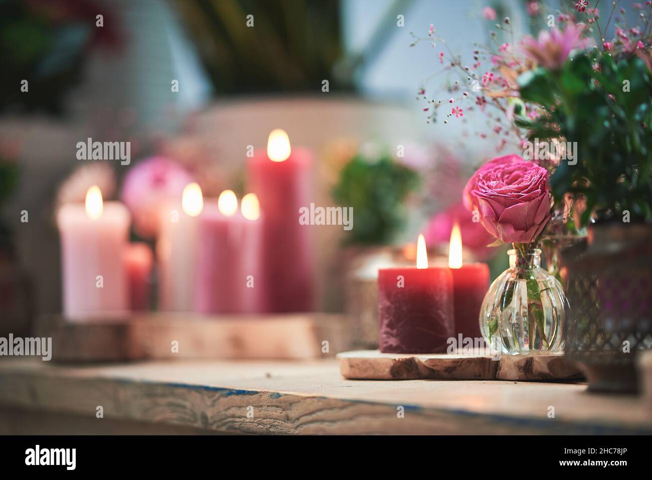 Fuoco selettivo di una rosa rosa in un piccolo bicchiere accanto alle piante e candele accese a una festa Foto Stock