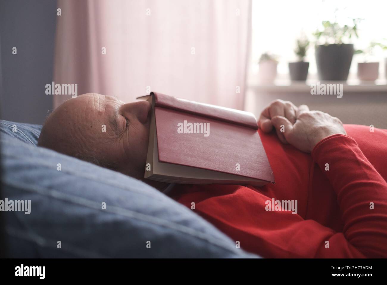 Uomo caucasico anziano che dorme con libro sul divano che peping dopo cena Foto Stock