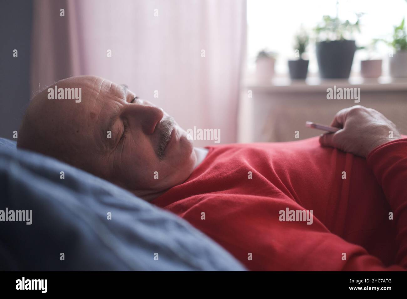 Uomo anziano che dorme avendo sogno dolce sul letto in camera da letto la mattina Foto Stock