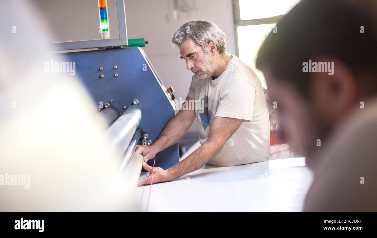 Due operatori tecnici lavorano su una macchina da stampa termica a rullo per sublimazione tessile industriale di alta qualità in digital printshop o Foto Stock