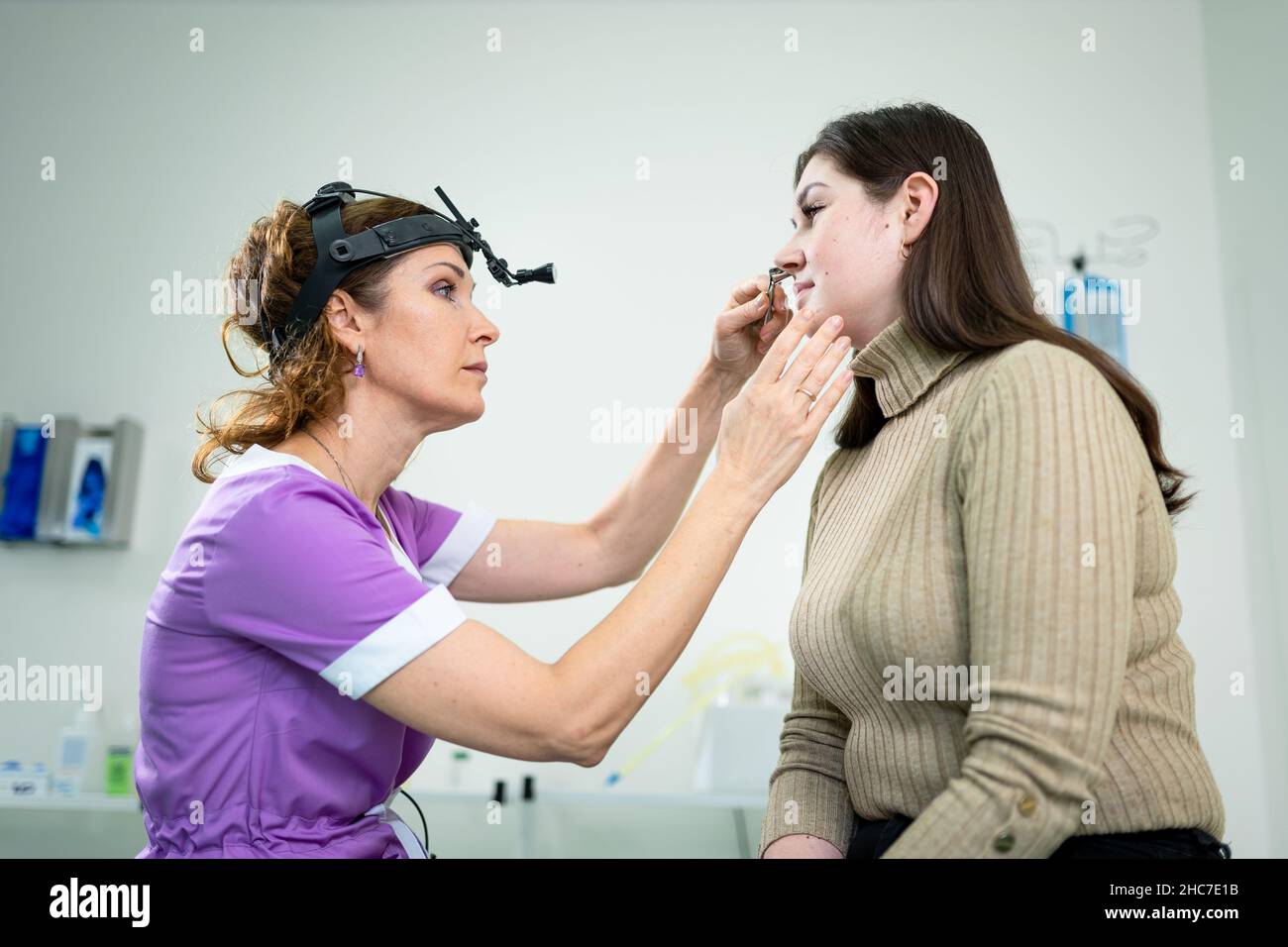 Concetto di otolaringologia. Otorhinolaringologist donna positiva che controlla il naso con otoscopio del suo paziente in ospedale. Congestione nasale, sinusite Foto Stock