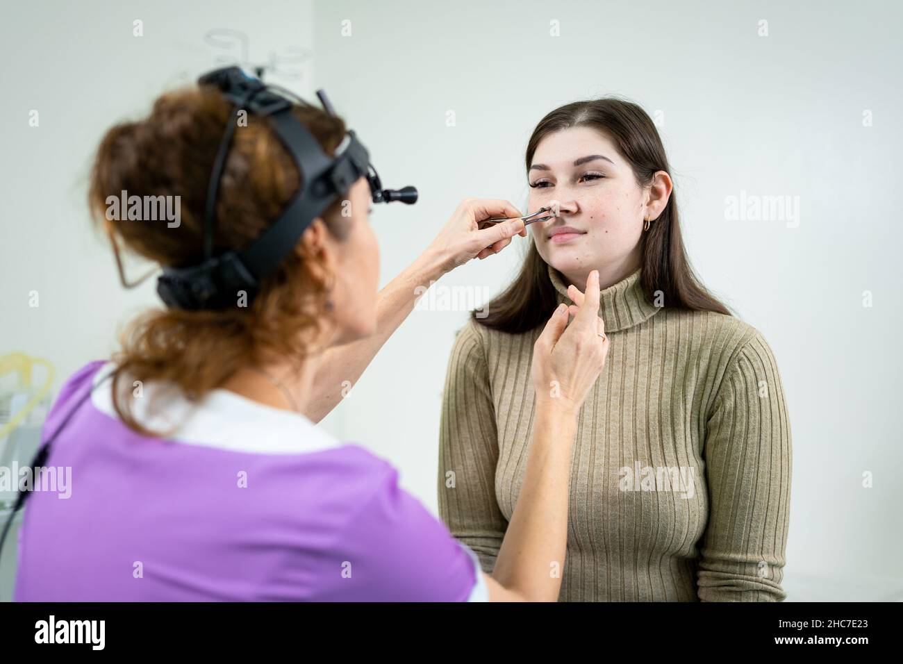 Concetto di otolaringologia. Otorhinolaringologist donna positiva che controlla il naso con otoscopio del suo paziente in ospedale. Congestione nasale, sinusite Foto Stock