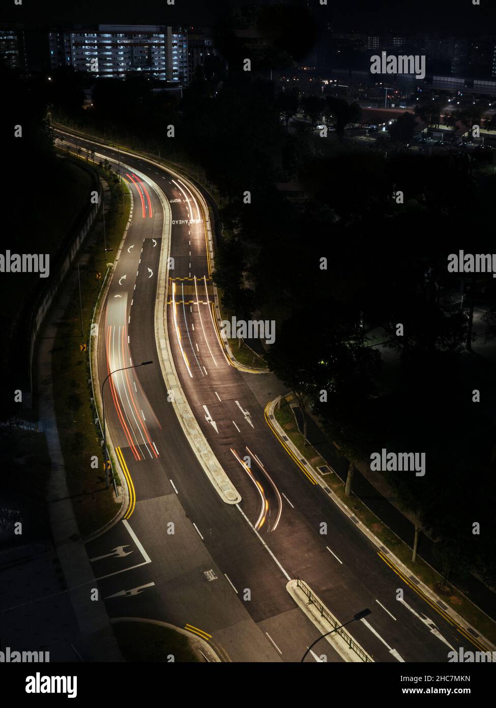 strada curva illuminata contro foresta scura con la città Foto Stock