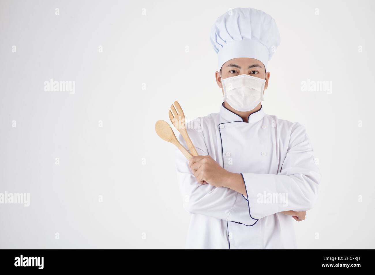 Ritratto dello chef del ristorante in uniforme bianca e maschera medica con spatole di cucina in legno Foto Stock
