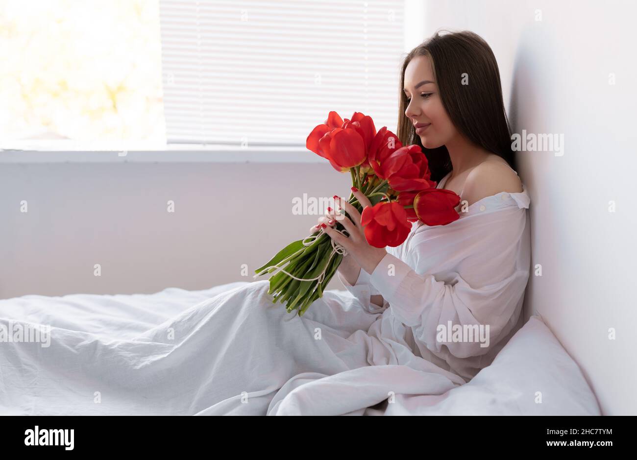 giovane bella donna al mattino in camera da letto si siede con un grande bouquet di tulipani. fiori a una donna per anniversario, san valentino, o solo Foto Stock