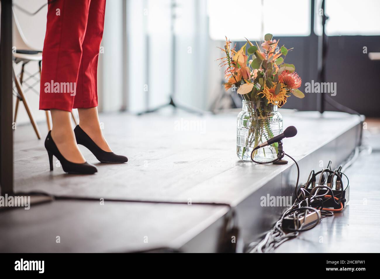 Gambe della donna visibili su un palco accanto ad un vaso glassoso di fiori diversi Foto Stock