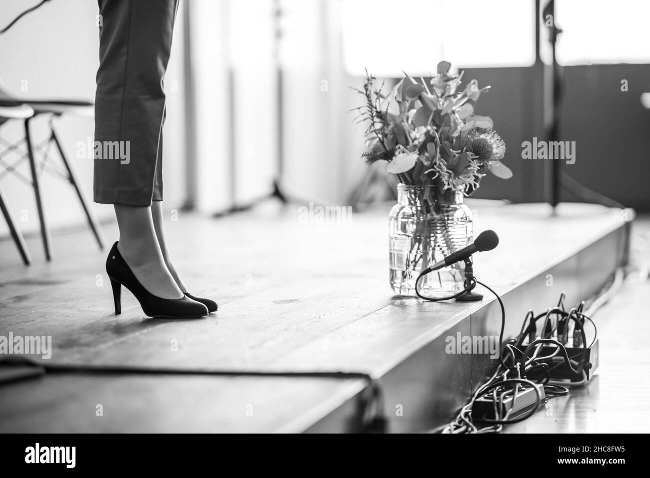 Immagine in scala di grigi delle gambe di una donna visibile su un palco accanto all'attrezzatura musicale e a un vaso di fiori vetrificati Foto Stock