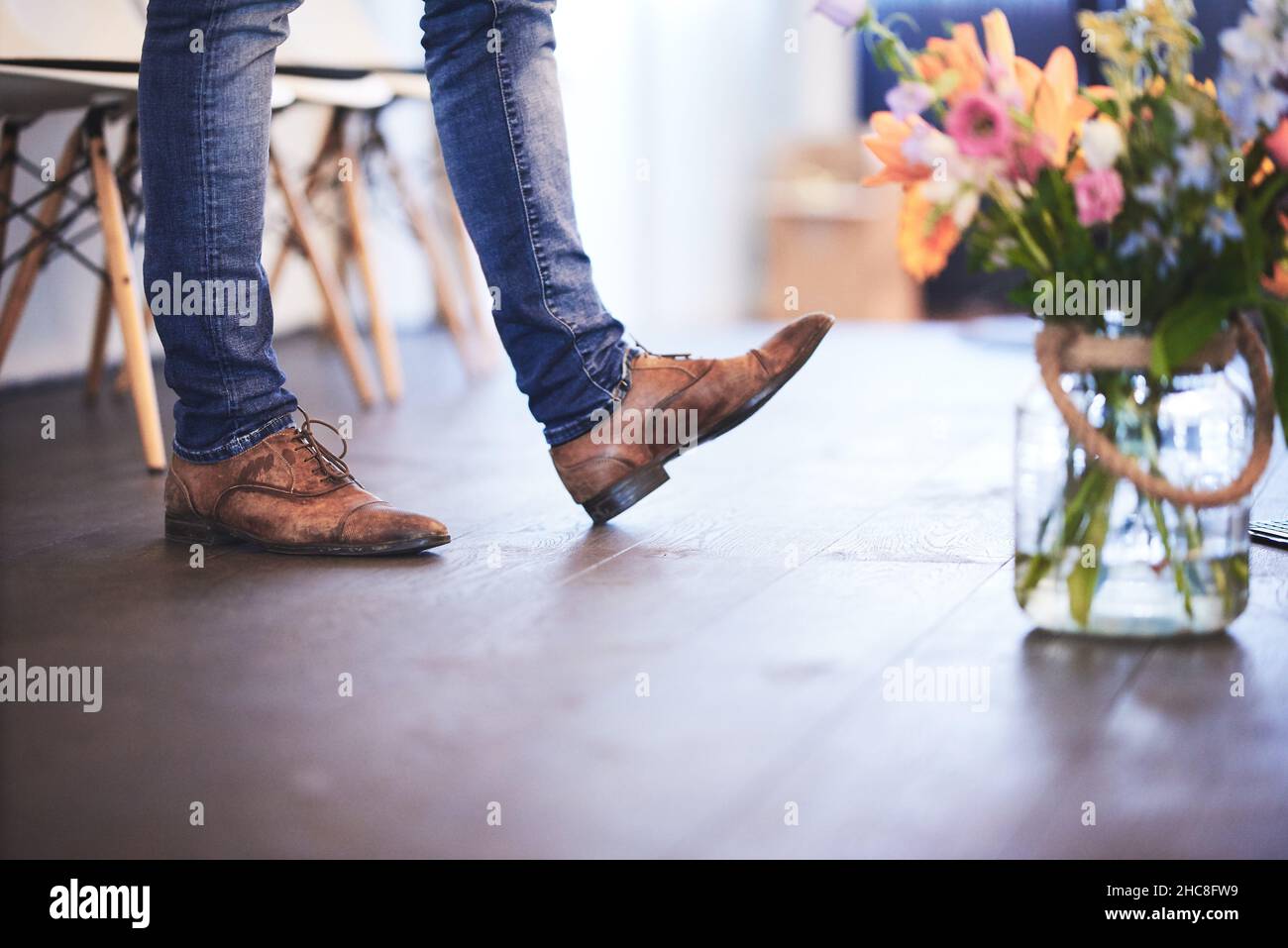 Gambe dell'uomo visibili su un palco accanto ad un vaso glassoso di fiori diversi Foto Stock