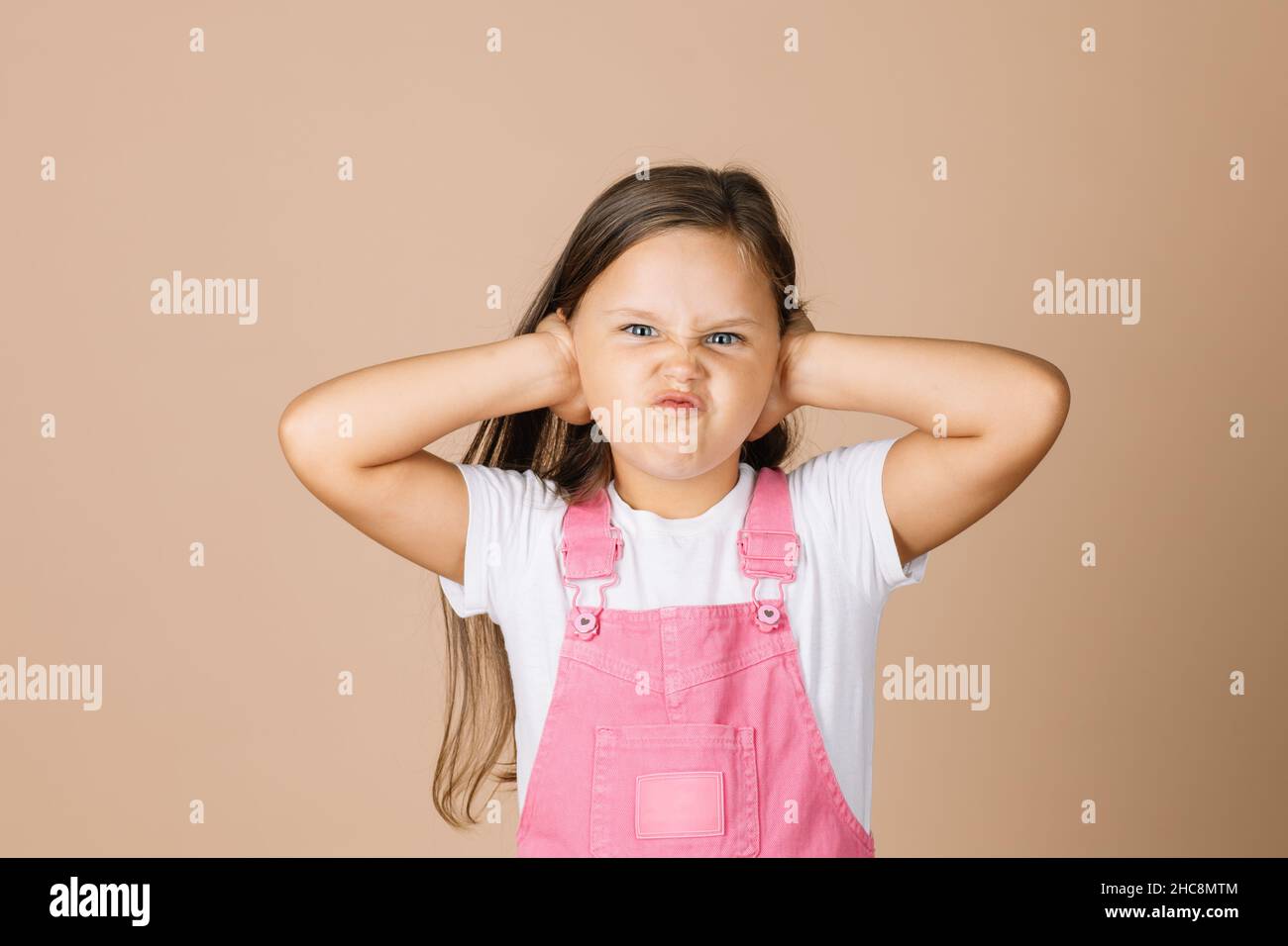 Ritratto foto di bambino che chiude le orecchie con le mani non sentire quello che gli altri dicono con frange-faccia con occhi luminosi guardando la fotocamera che indossa rosa brillante Foto Stock