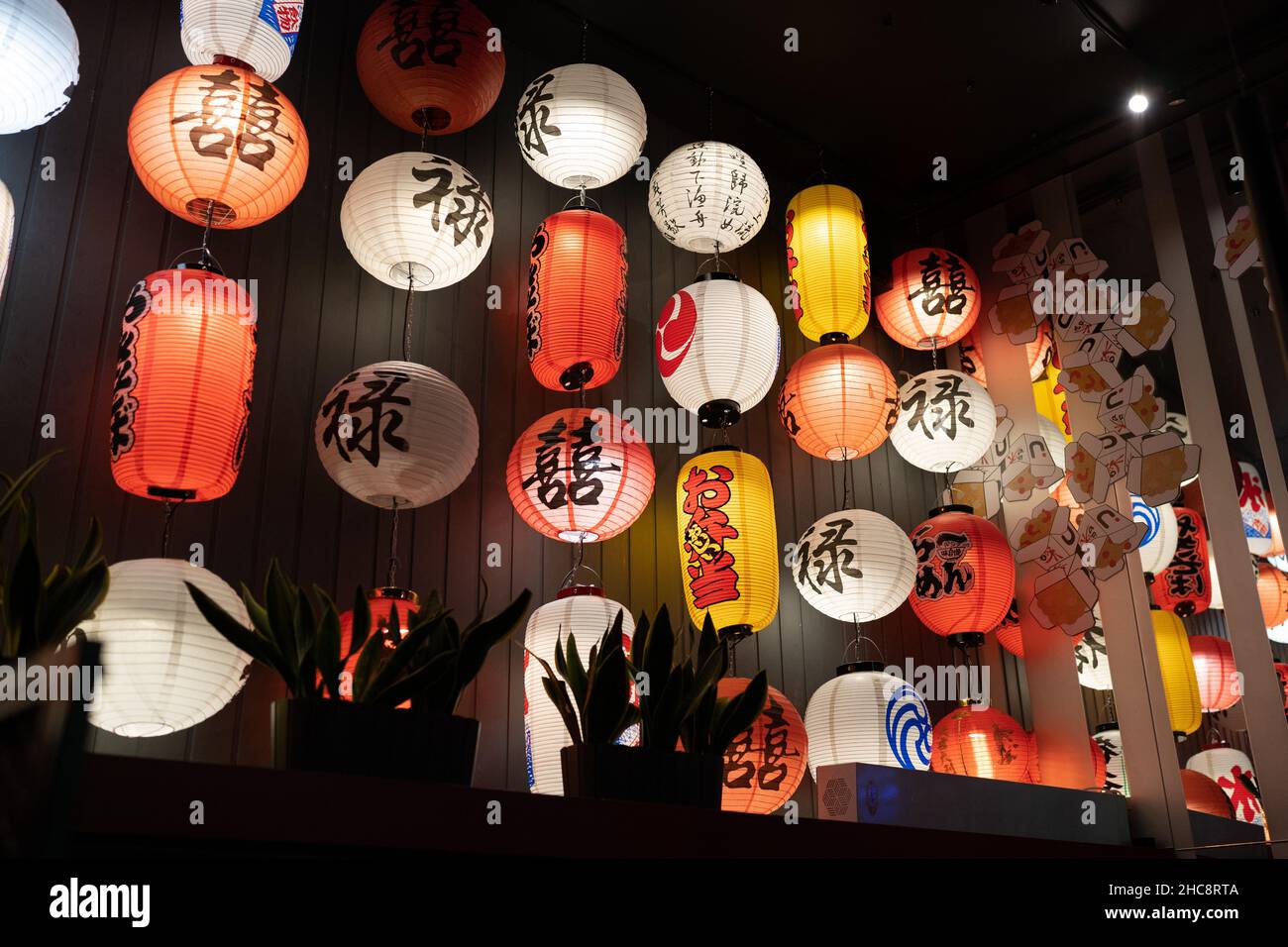 Le tradizionali lanterne cinesi si illuminano all'interno di un ristorante asiatico. Decorazioni su carta in un caffè alla moda Foto Stock