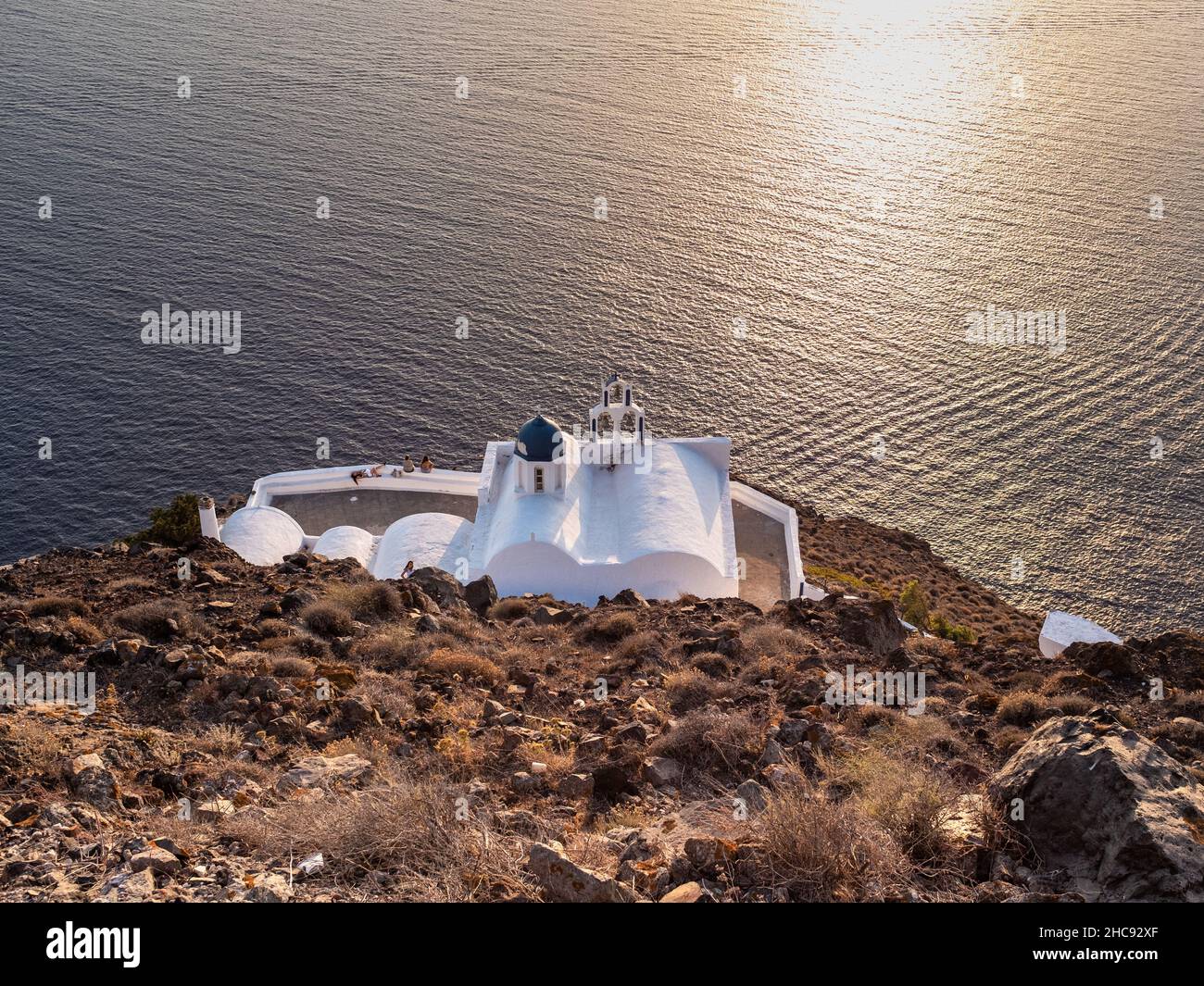 Santorini, Grecia - 28 luglio 2021: Una tipica chiesa greca ortodossa che si affaccia sul Mar Egeo con il sole che si riflette sulla superficie del mare. Preso alla e Foto Stock