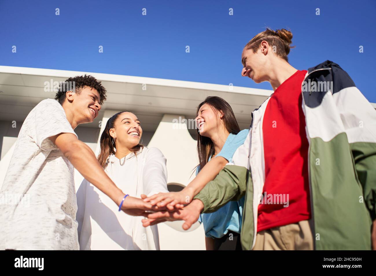 Gruppo di giovani che si accatastano le mani celebrando i successi. Ritratto di studenti multietnici ridendo nel campus universitario. Foto Stock