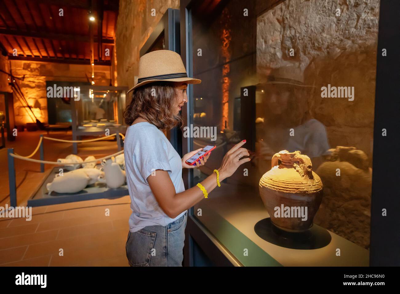 Donna visitatore che utilizza lo smartphone con l'app audio-guida per conoscere i manufatti e le mostre dell'antica grecia Foto Stock