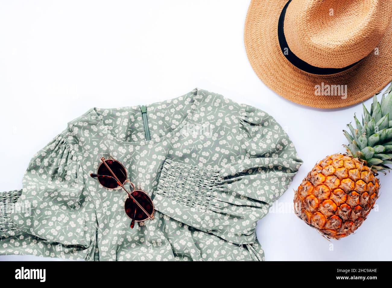 Stile casual estivo. Abiti e accessori eleganti da donna. Abito, occhiali da sole, cappello e ananas su sfondo bianco. Disposizione piatta, vista dall'alto. Foto Stock