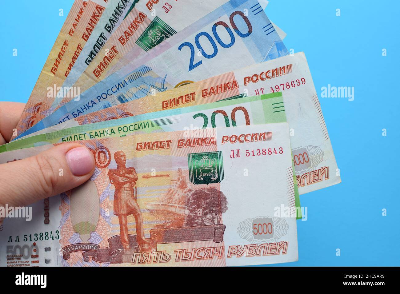 Banconote rubli russe in una mano femminile su sfondo blu. Foto Stock