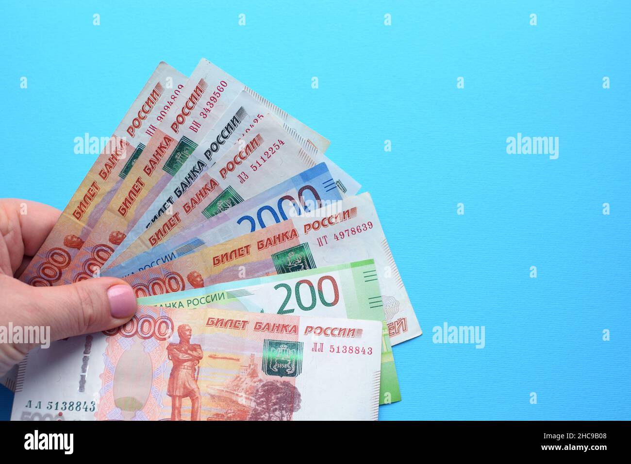 Banconote rubli russe in una mano femminile su sfondo blu. Foto Stock
