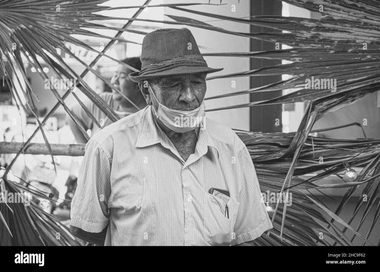 Foto in scala di grigi di un vecchio maschio che indossa una maschera medica e un cappello a Koh Phangan, Thailandia Foto Stock