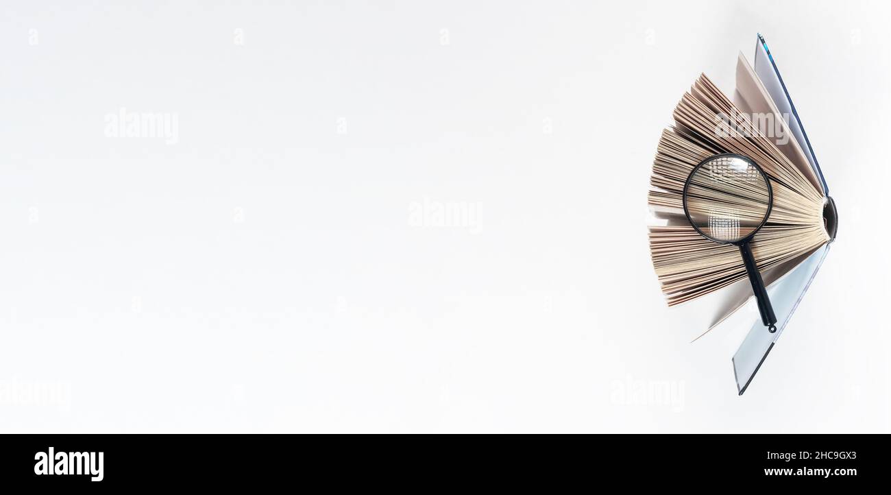 Lente di ingrandimento sopra il libro di carta aperto. Concetto di conoscenza, ricerca e studio. Banner con spazio di copia. Foto Stock