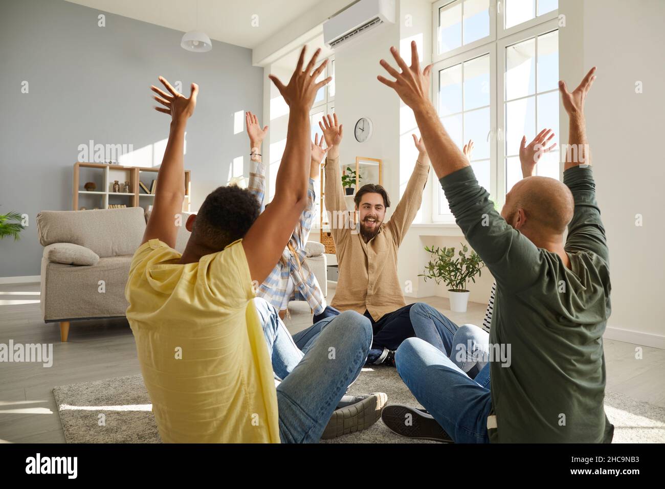 Gruppo di amici motivati si siedono sul pavimento in cerchio e alzano le mani godendo il tempo di divertimento insieme. Foto Stock