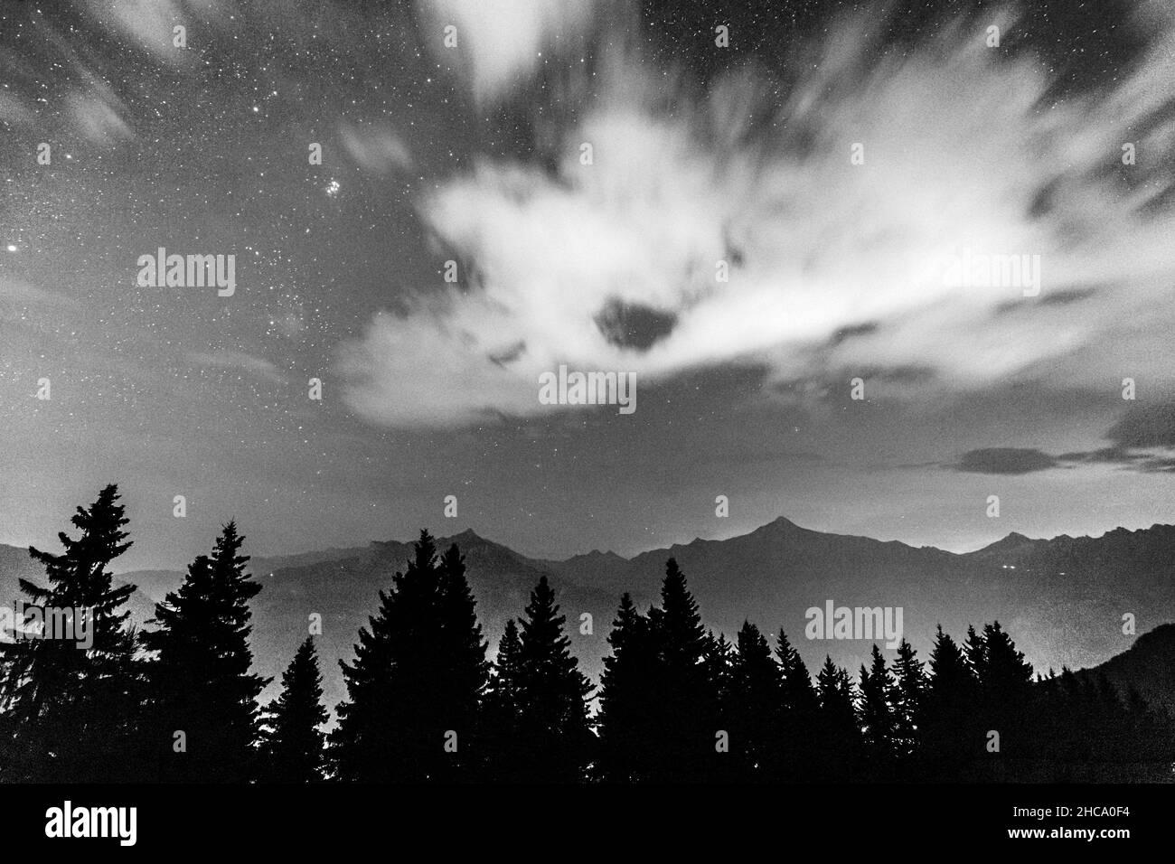 Foto in scala di grigi della Via Lattea e stelle nel cielo della sera su un paesaggio con alberi in Austria Foto Stock