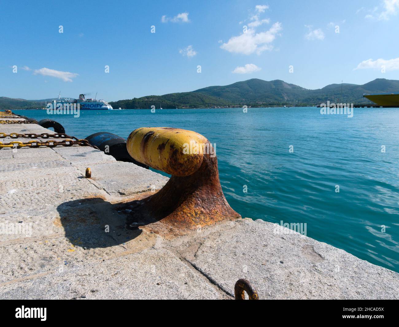 Primo piano di un arrugginito vecchio giallo Bollard Dew Maritime dalle acque blu in una giornata di sole Foto Stock