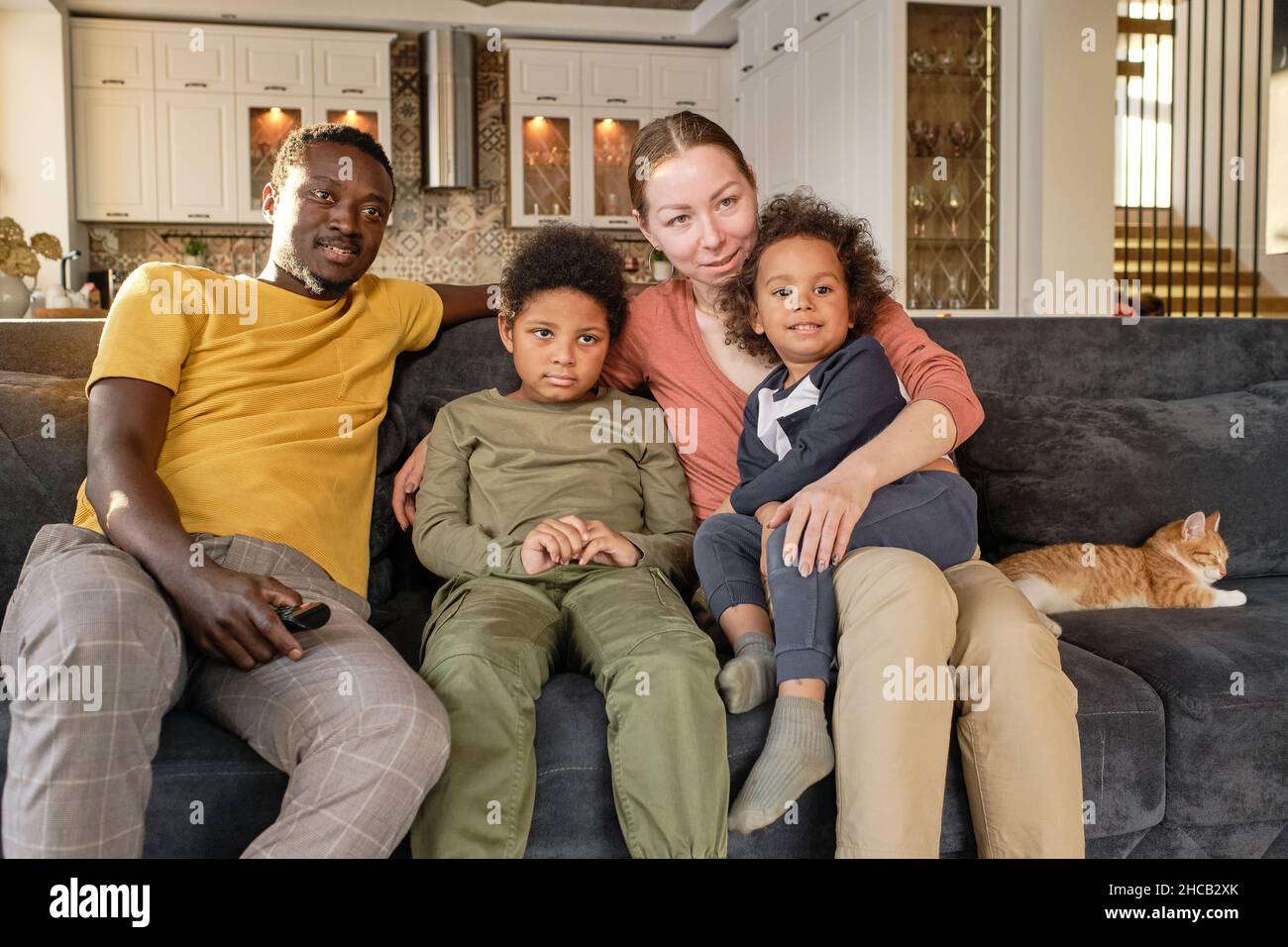 Una famiglia giovane e affettuosa seduta sul divano e guardando i film sul televisore mentre si soggiorna a casa e si riposa Foto Stock