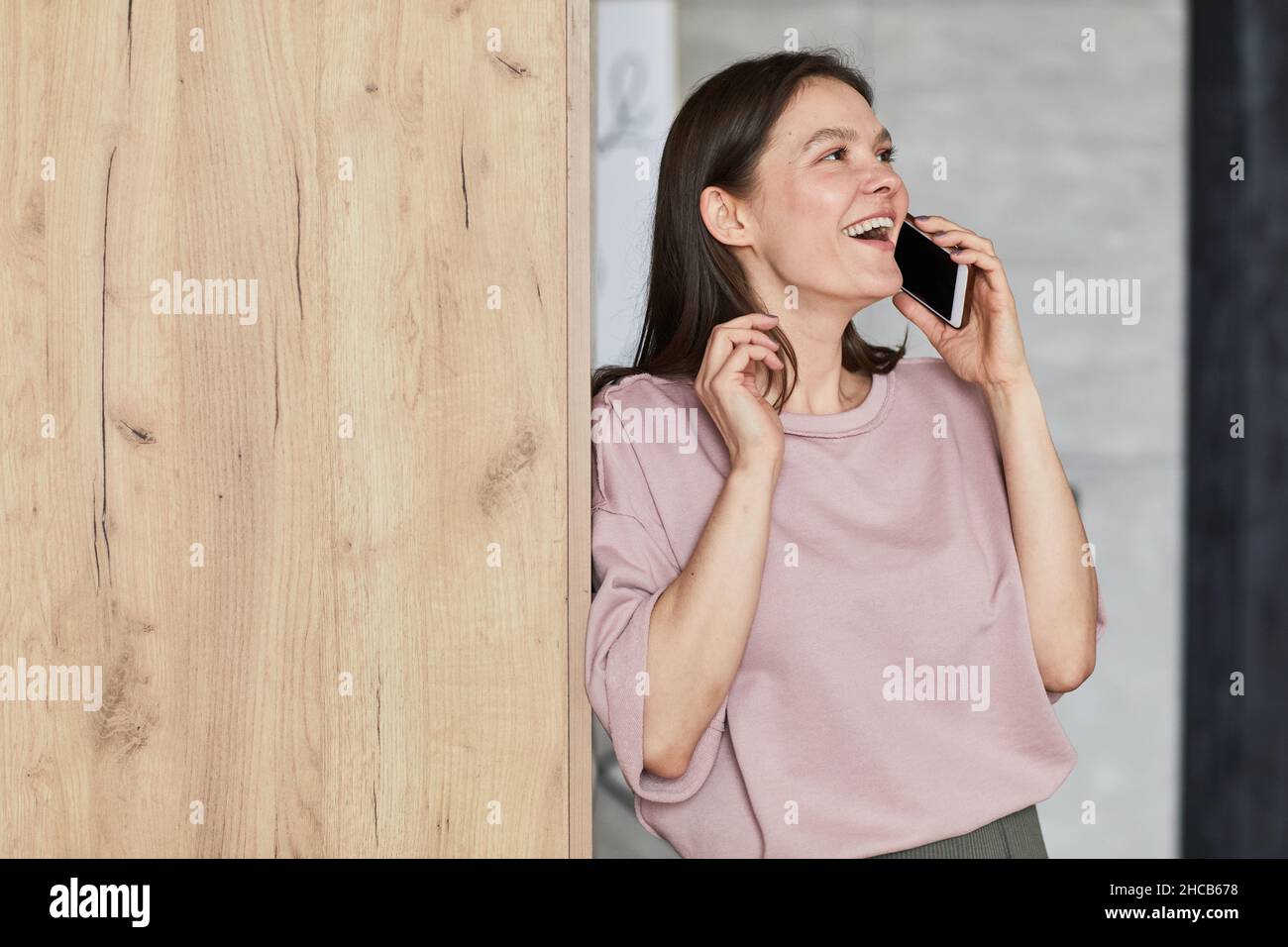 Felice giovane donna appoggiata sul muro parlando sul cellulare e ridendo durante la conversazione Foto Stock