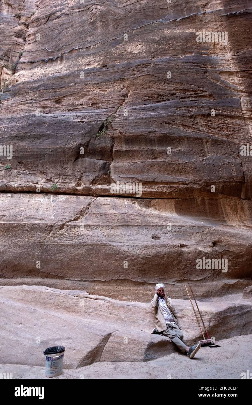 Un pulitore funzionante prende una pausa di sigaretta e telefono cellulare nell'antica città giordana di Petra. Foto Stock