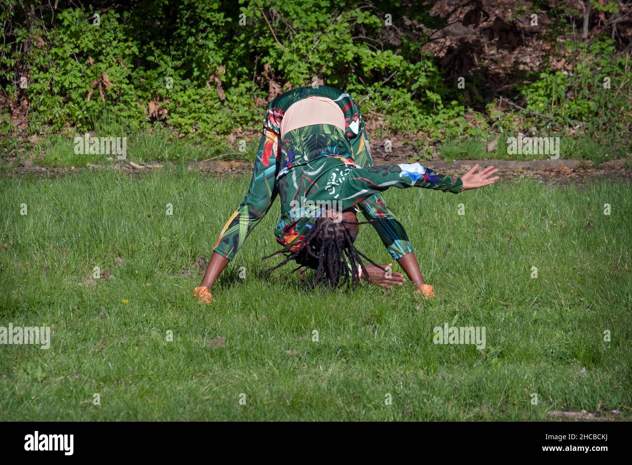 Una donna fit agile negli anni '50 in una lezione di yoga meditativa in un parco a Flushing, Queens, New York City. Foto Stock