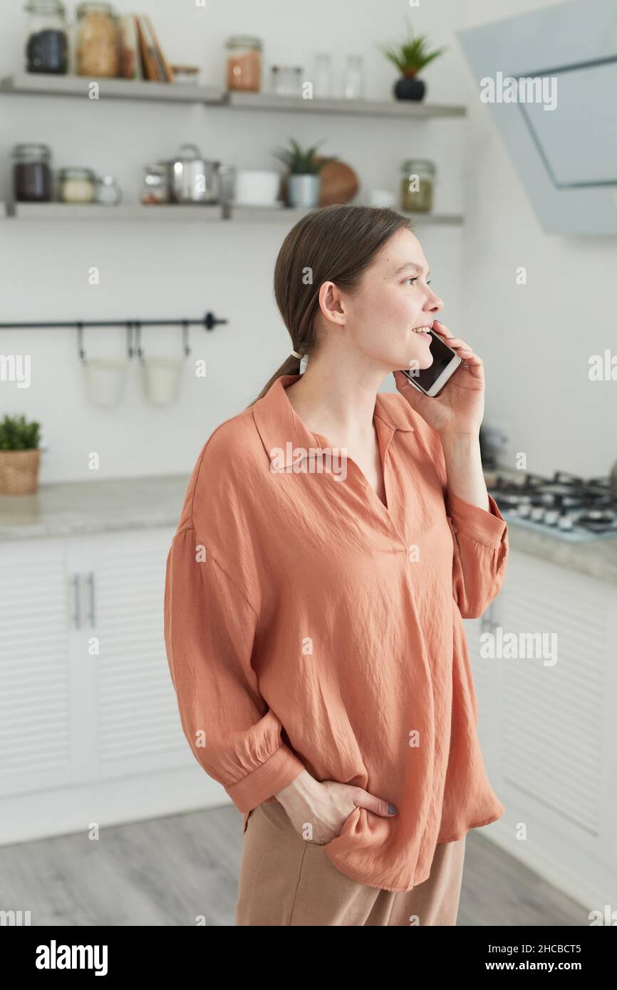 Giovane donna che ha una conversazione di lavoro sul telefono cellulare mentre si trova in cucina Foto Stock