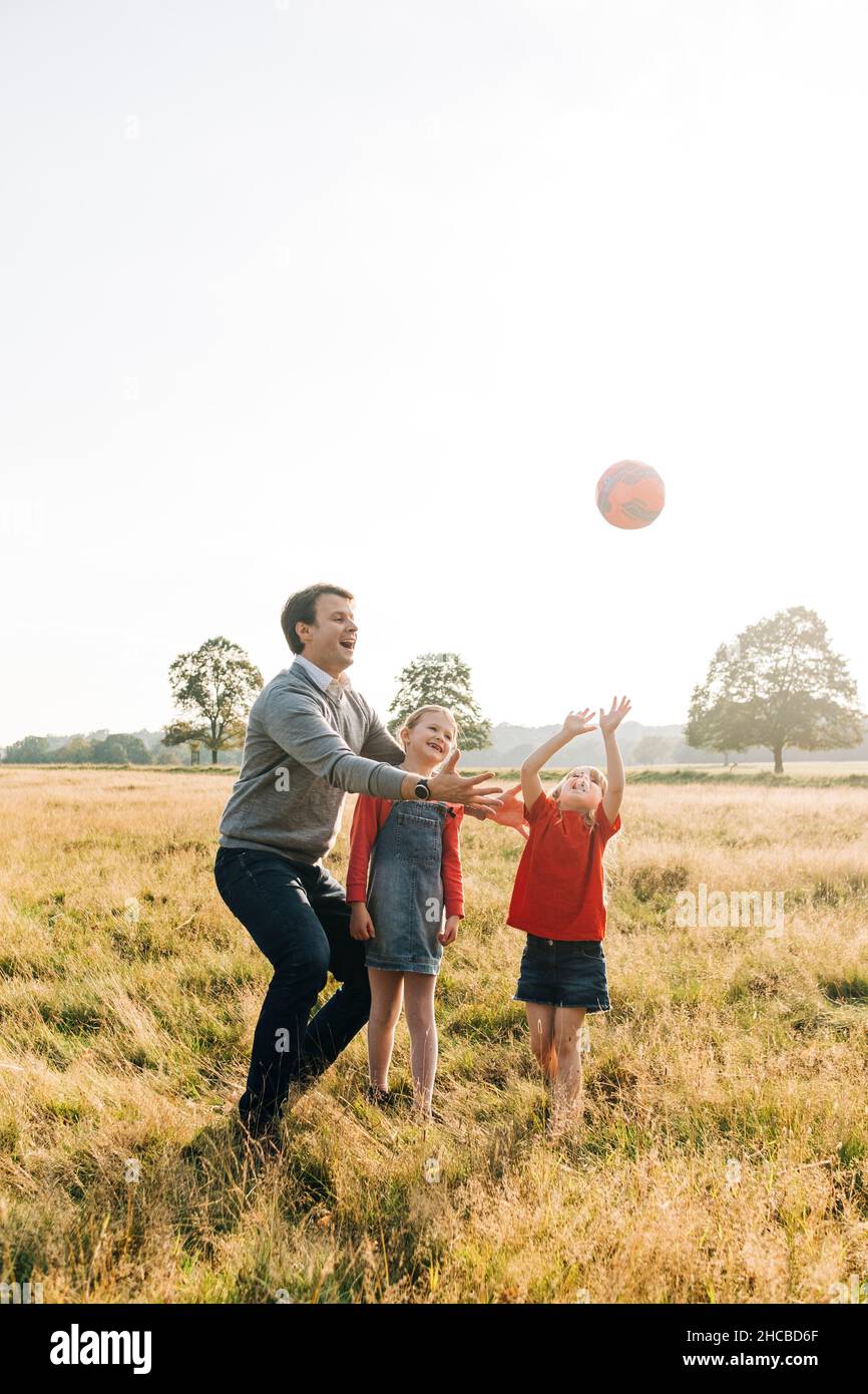 Padre e figlie che giocano con la palla nel parco Foto Stock