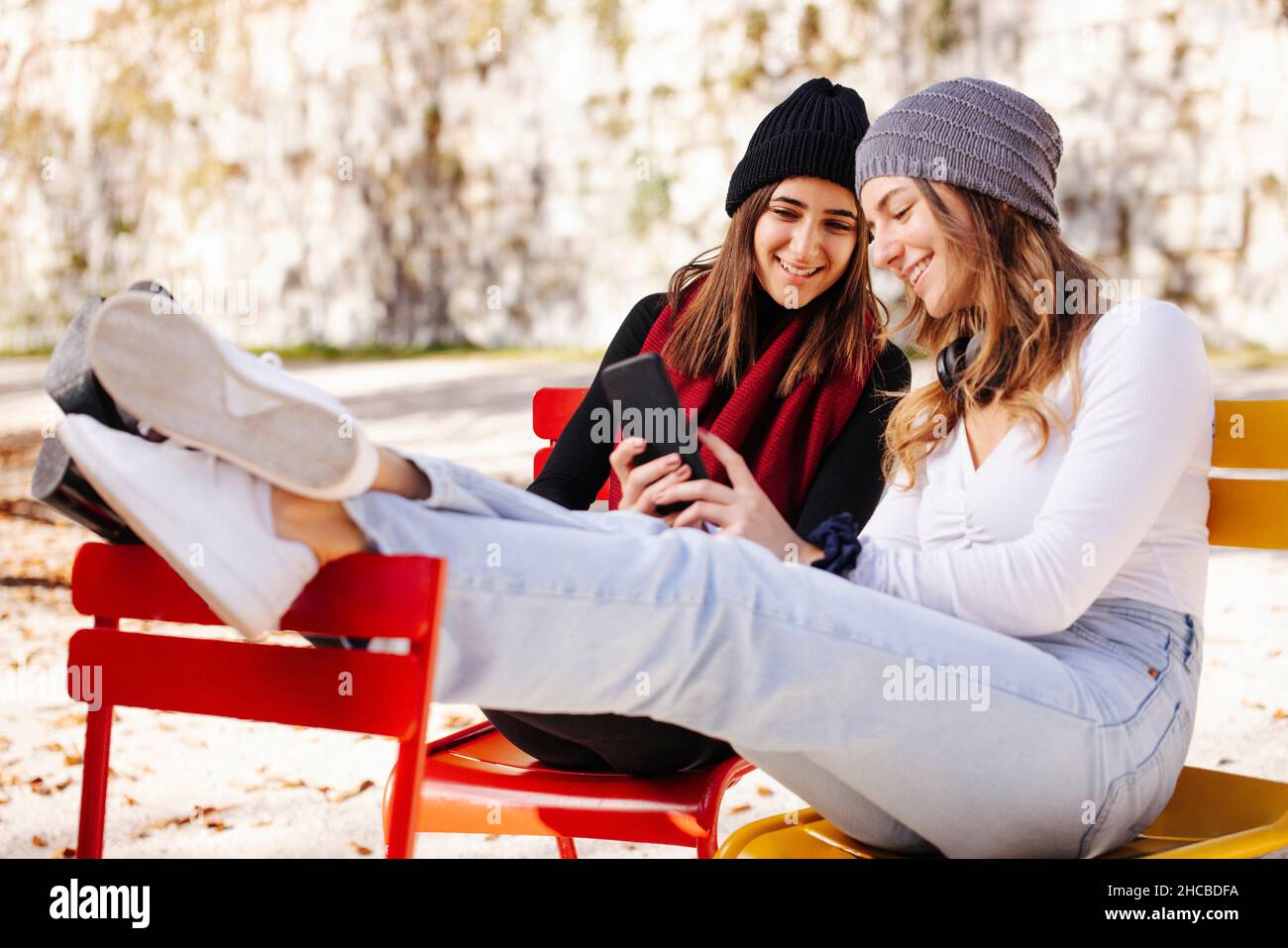 Sorridente ragazza che condivide il telefono cellulare con un amico il giorno di sole Foto Stock