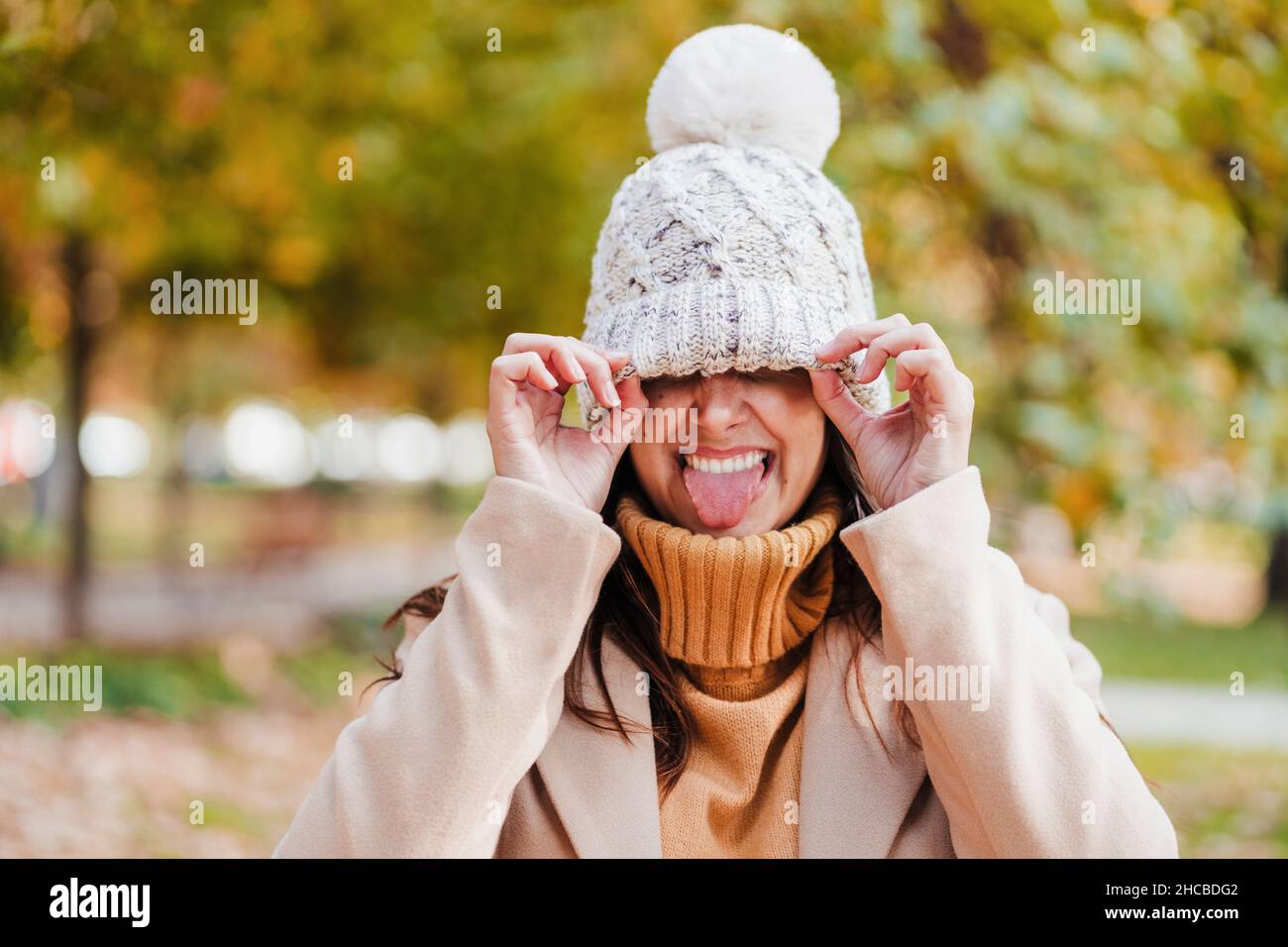 Donna giocosa con cappello a maglia che attacca la lingua al parco Foto Stock