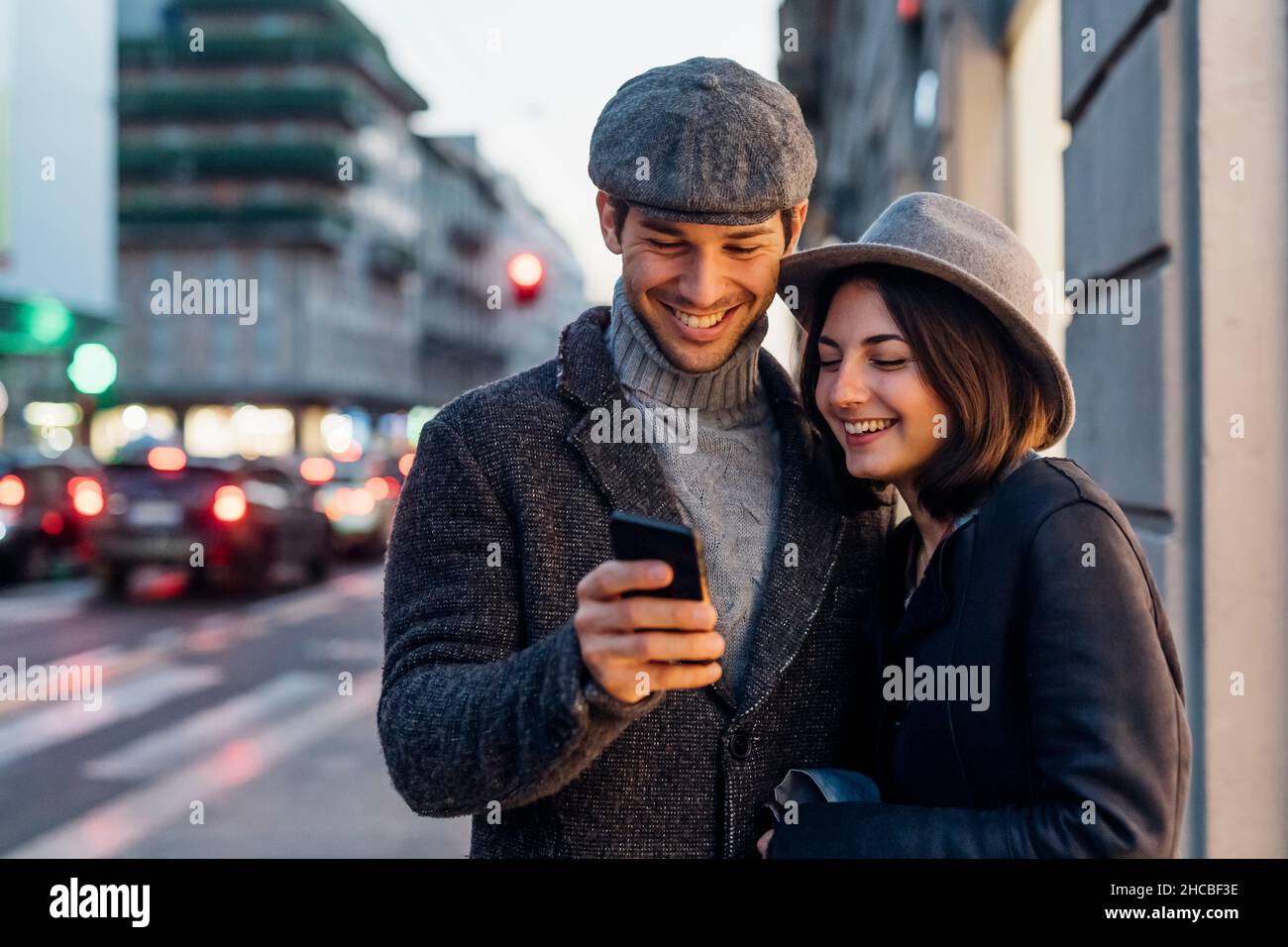 Coppia felice in abiti caldi che condividono lo smart phone sulla strada Foto Stock