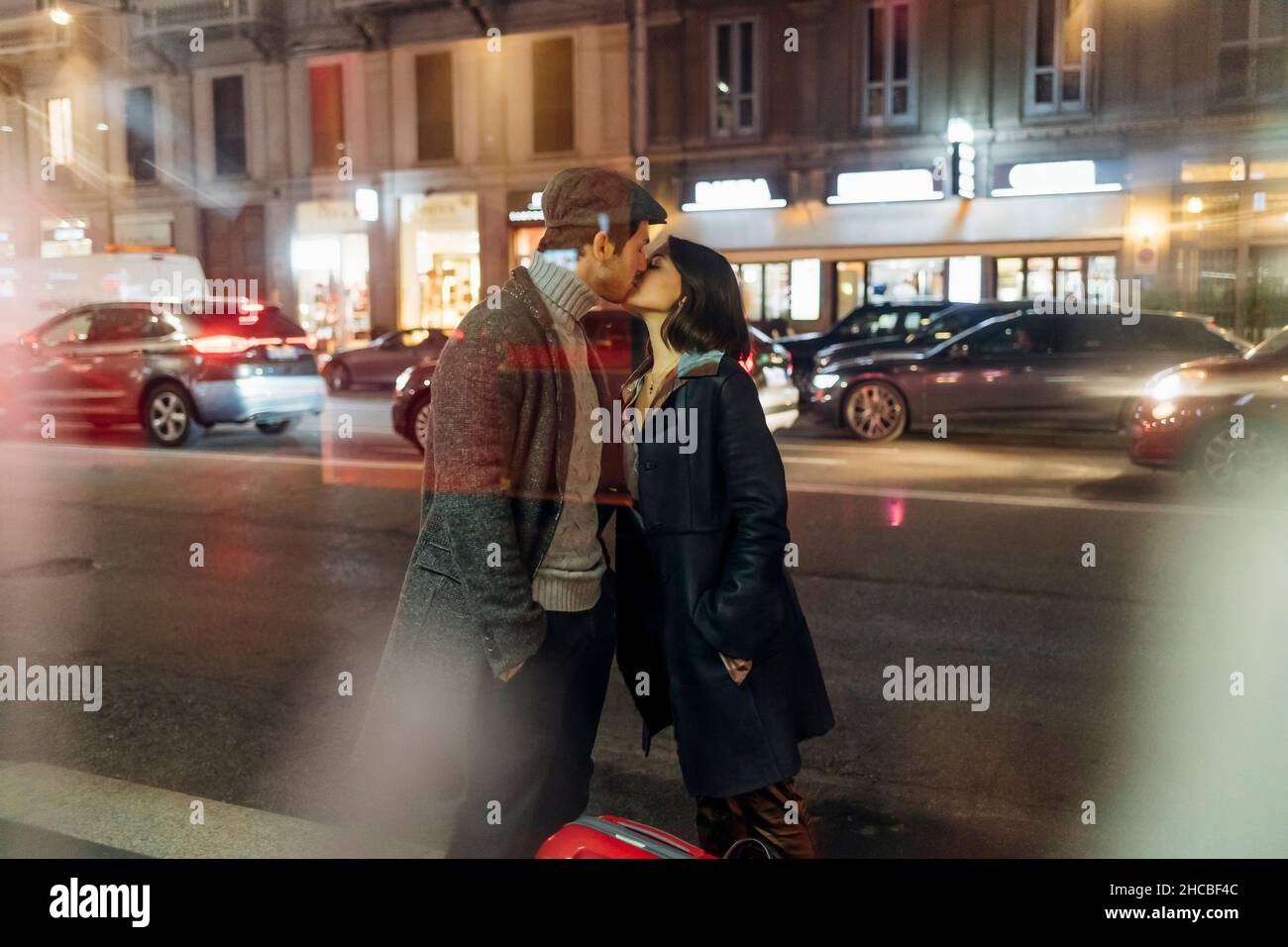 Giovane coppia in abiti caldi bacia sulla strada illuminata della città Foto Stock