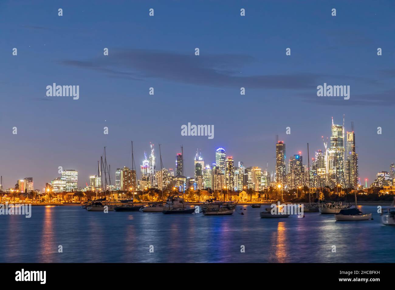 Australia, Victoria, Melbourne, Yachts galleggiano contro lo skyline illuminato della città al tramonto Foto Stock