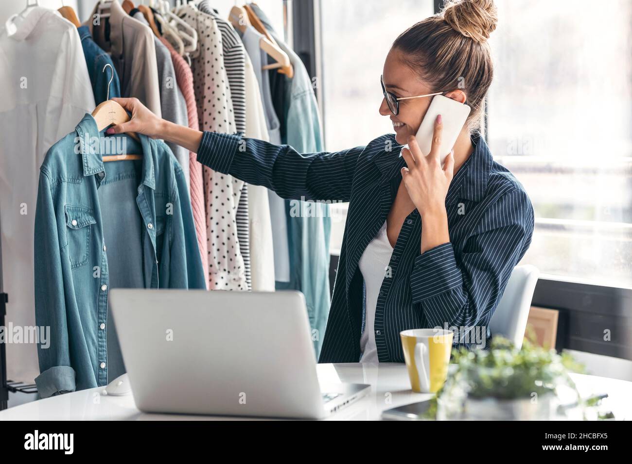 Stilista di moda che tiene la camicia e parla sul telefono cellulare in ufficio Foto Stock