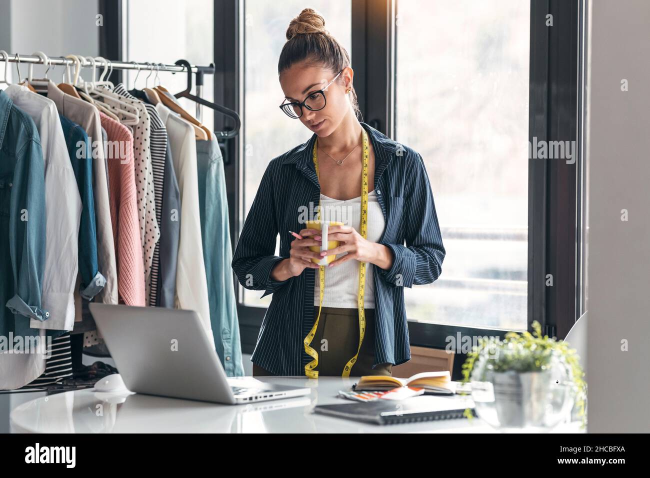 Stilista di moda con tazza da caffè utilizzando il computer portatile in ufficio Foto Stock